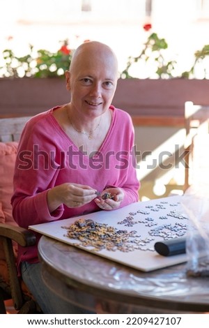 Woman undergoing chemotherapy treatment for breast cancer assembles a puzzle on the terrace of her house