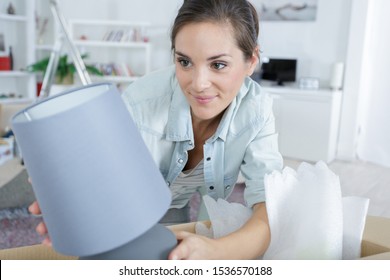 Woman Unpacking Lamp From Cardboard Box In Her New Home