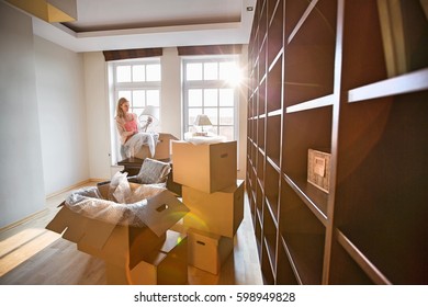 Woman Unpacking Lamp From Moving Box At New House