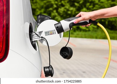 Woman Unplugging A Charger From An Electric Car Socket. Eco Friendly Vehicle With Zero Emission 