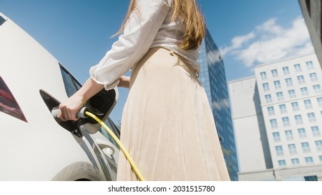 Woman Unplugging The Electric Car Charger At A Downtown Charging Point