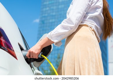 Woman unplugging the electric car charger at a downtown charging point