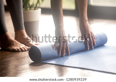 Woman unrolling blue yoga mat to perform yoga asanas safely and comfortably, preparing for working out in fitness club, before or after sport routine, legs and hands close up view. Well being concept