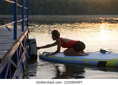A woman untying her paddleboard for her morning yoga on a calm beautiful river