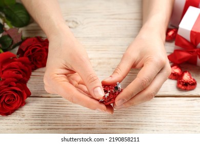 Woman Unwrapping Heart Shaped Chocolate Candy At White Wooden Table, Closeup