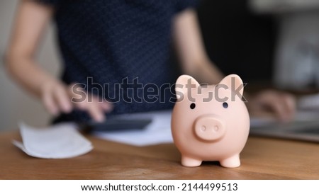 Woman use calculator, manage family budget, calculates personal expenses, control incomes, close up focus on piggy bank moneybox, as symbol of economy, savings control, take care of tomorrow concept