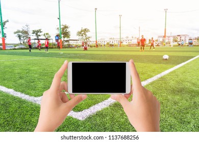 Woman Use Mobile And The Asian Kids Football Match On The Artificial Football Field