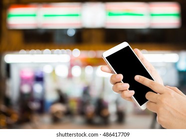 Woman Use Mobile Phone And Blurred Image Of People In Front Of The Convenience Store At Night