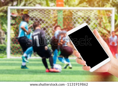 woman use mobile phone and blurred image of asian boys soccer game