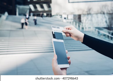 Woman Use Of Mobile Phone To Pay. Swiping Credit/Debit Card With Card Reader Outdoors In The City