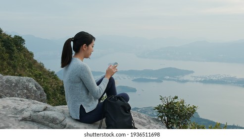 Woman use of mobile phone and sit at the top of mountain