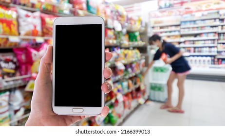 Woman use mobile phone,blur image of a girl choosing snacks in a convenience store as background.