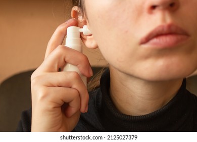 Woman uses an ear spray. Nozzle is installed in the ear hole. Daily hygiene and care of the ear canal. Horizontal photo.