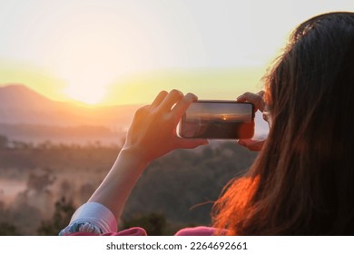 A woman uses her smartphone to take pictures of the sunrise in a valley with abundant nature tourism and technology.