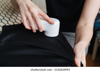 woman uses a machine for removing pellet and spools from clothes and fabric on black trousers. A modern electronic device for updating old things.