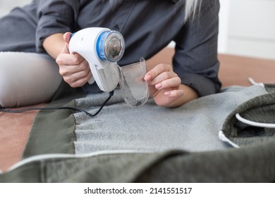 woman uses a machine for removing pellet and spools from clothes and fabric on black trousers. A modern electronic device for updating old things