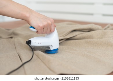 woman uses a machine for removing pellet and spools from clothes and fabric on black trousers. A modern electronic device for updating old things.