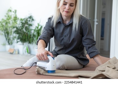 woman uses a machine for removing pellet and spools from clothes and fabric on black trousers. A modern electronic device for updating old things - Shutterstock ID 2254841441