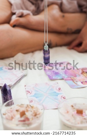 a woman uses the pendulum on oracle cards in a lit altar with pr