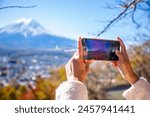 Woman uses a smartphone to take pictures of Mount Fuji in autumn.