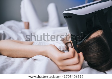 Woman uses virtual reality glasses at home on the bed. Plays games, technologies of the future