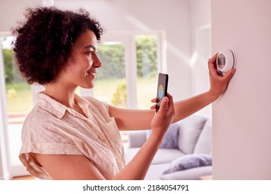 Woman Using App On Mobile Phone To Control Central Heating Thermostat At Home - Shutterstock ID 2184054791