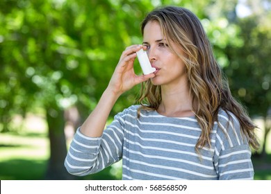 Woman using asthma inhaler in a park - Powered by Shutterstock