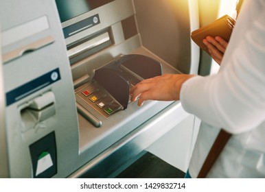 Woman using ATM holding wallet an pressing the PIN security number on the keyboard automatic teller machine