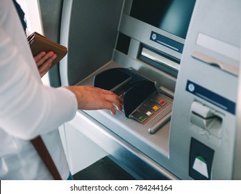 Woman using ATM holding wallet an pressing the PIN security number on the keyboard automatic teller machine 