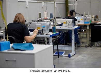 Woman using automatic sewing machine in handicraft workshop. Seamstress working on a loom in a textile factory, holding fabric while working - Powered by Shutterstock