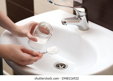 Woman Using Baking Soda To Unclog Sink Drain In Bathroom, Closeup