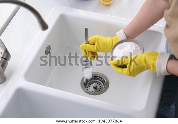 Woman\
using baking soda to unclog sink drain,\
closeup