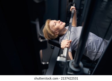 Woman Using Barbell Press Bench Machine In Gym