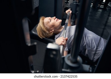 Woman Using Barbell Press Bench Machine In Fitness Club