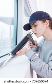 Woman Using Caulking Gun Around Window