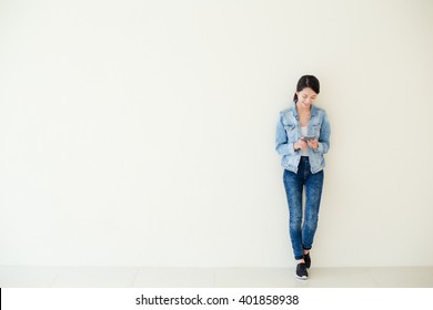 Woman using cellphone and standing against big wall 