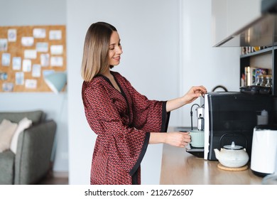 Woman using coffee machine to make big mug of coffee at home. Woman wearing silk robe at home while preparing a latte