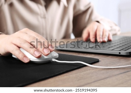Woman using computer mouse while working with laptop at wooden table, closeup