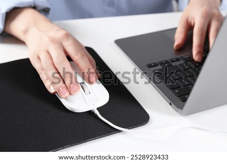 Woman using computer mouse while working with laptop at white table, closeup