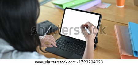 The woman is using a computer tablet and stylus pen at the wooden working table.