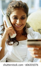 Woman Using Cordless Phone And Looking At Credit Card