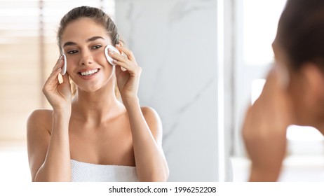 Woman Using Cotton Pads Cleaning Face With Micellar Water Caring For Skin Looking At Mirror Standing In Modern Bathroom At Home. Young Lady Enjoying Facial Skincare Routine Concept. Panorama