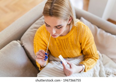 woman using cotton swab while doing coronavirus PCR test at home. Woman using coronavirus rapid diagnostic test. Young woman at home using a nasal swab for COVID-19. - Shutterstock ID 1967366755