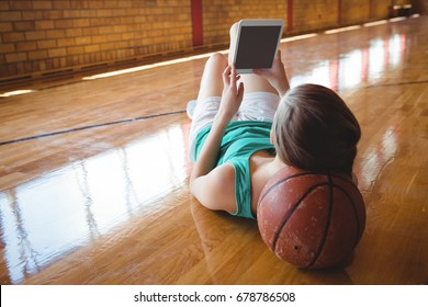 Woman using digital tablet while lying on floor in basketball court - Powered by Shutterstock