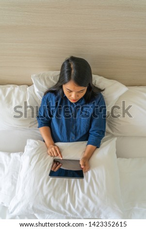 Woman using digital tablet with white pillow on the bed