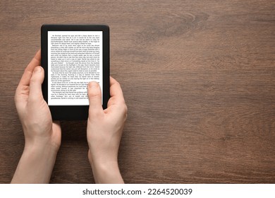 Woman using e-book reader at wooden table, top view. Space for text