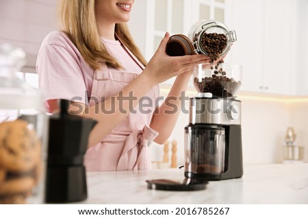 Woman using electric coffee grinder in kitchen, closeup
