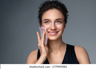 Woman using facial oil blotting paper. Photo of woman with perfect makeup on gray background. Beauty concept