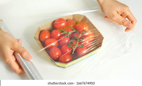 Woman using food film for food storage on a white table. Roll of transparent polyethylene food film for packing products.