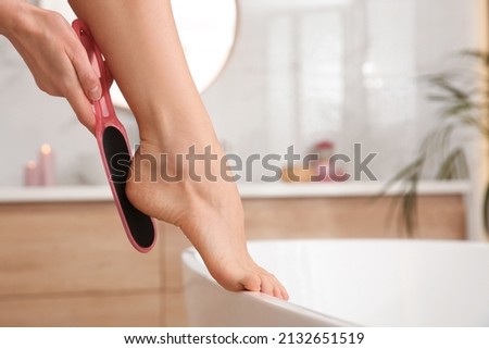 Woman using foot file for removing dead skin from feet in bathroom, closeup